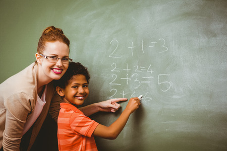 Portrait of teacher assisting little boy to write on blackboard in the classroomの写真素材