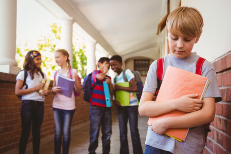 Portrait of sad schoolboy with friends in background at school corridorの写真素材