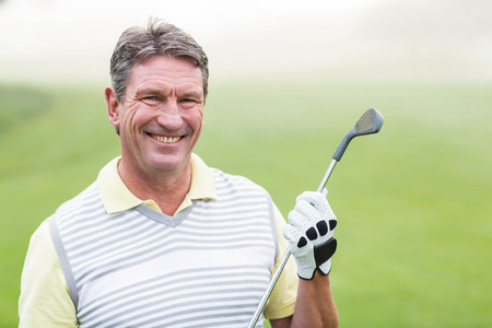 Cheerful golfer smiling at camera holding his club on a foggy day at the golf courseの写真素材