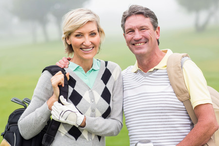 Golfing couple smiling and holding clubs on a foggy day at the golf courseの写真素材