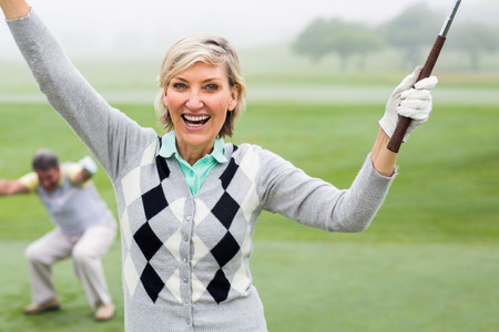 Lady golfer cheering at camera with partner behind on a foggy day at the golf courseの写真素材