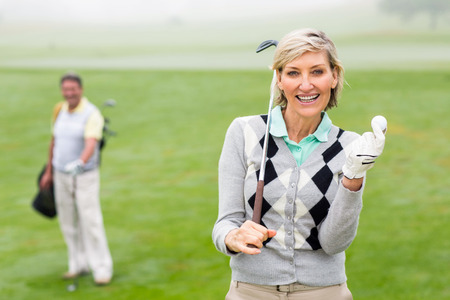 Lady golfer smiling at camera with partner behind on a foggy day at the golf courseの写真素材