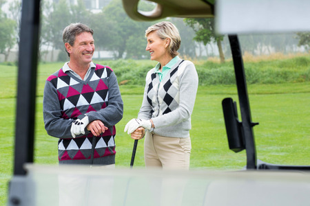 Happy golfing couple laughing on a foggy day at the golf courseの写真素材