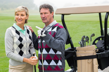 Happy golfing couple with golf buggy behind on a foggy day at the golf courseの写真素材