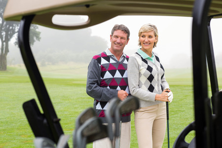 Happy golfing couple smiling on a foggy day at the golf courseの写真素材