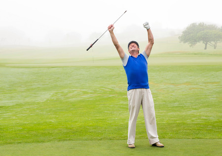 Excited golfer cheering on putting green on a foggy day at the golf courseの写真素材