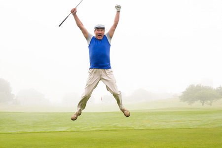 Excited golfer jumping up and smiling at camera on a foggy day at the golf courseの写真素材