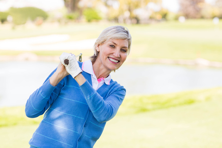 Female golfer standing holding her club smiling on a sunny day at the golf courseの写真素材