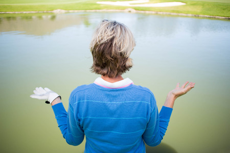 Confused female golfer looking at lake on a sunny day at the golf courseの写真素材