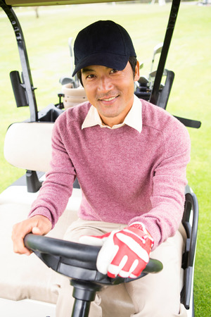 Happy golfer driving his golf buggy at the golf courseの写真素材