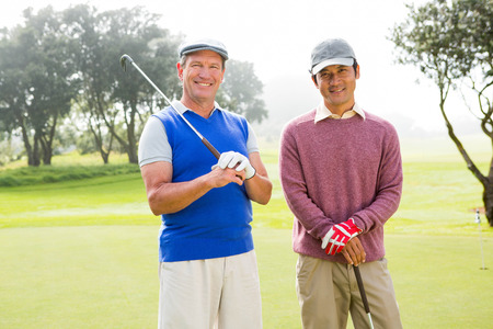 Golfing friends smiling at camera holding clubs at the golf courseの写真素材