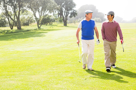 Golfer friends walking and chatting on a sunny day at the golf courseの写真素材