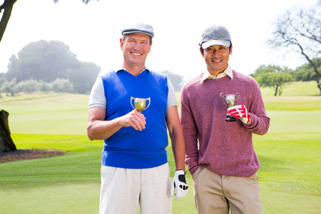 Golfing friends holding cups smiling at camera at golf courseの写真素材