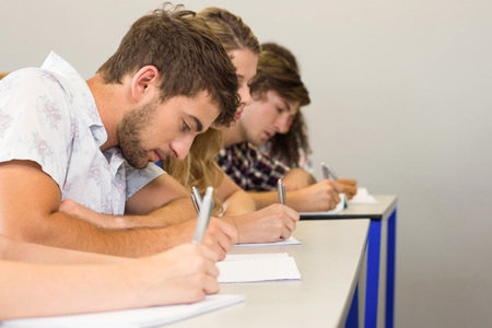 Side view of students writing notes in classroomの写真素材