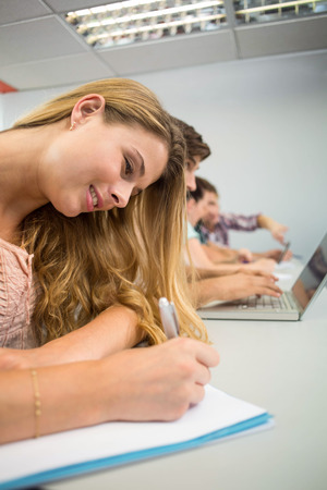 Side view of students writing notes in classroomの写真素材