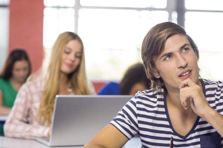 Thoughtful male student sitting in the classroomの写真素材