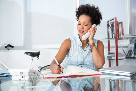 Beautiful young casual woman using telephone in officeの写真素材