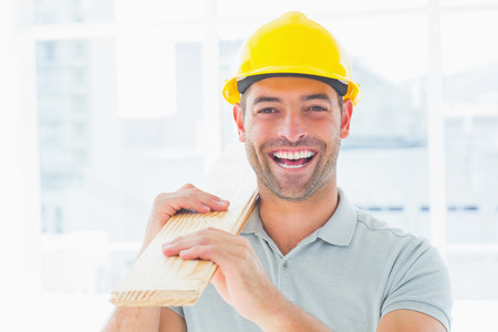 Portrait of cheerful male carpenter wearing hardhat while carrying planksの写真素材