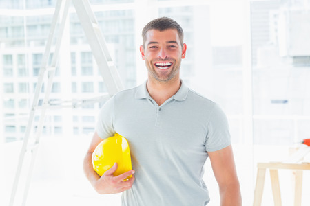 Portrait of cheerful handyman holding hardhat at construction siteの写真素材