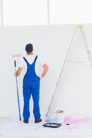 Full length rear view of handyman with paint roller examining wall at homeの写真素材