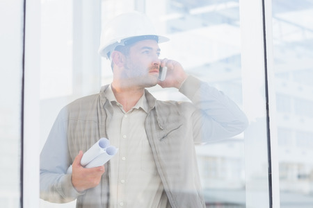 Male architect with blueprints using mobile phone in officeの写真素材