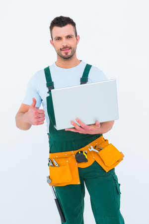 Smiling construction worker holding laptop on white backboardの写真素材