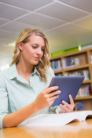 Pretty student studying in the library with tablet at the universityの写真素材