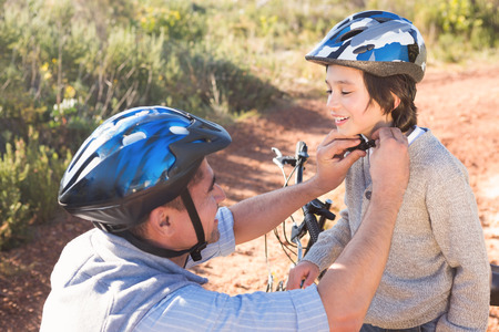 Father clipping on sons helmet on a sunny dayの写真素材