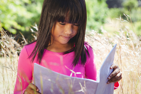Cute little girl reading in park on a sunny dayの写真素材