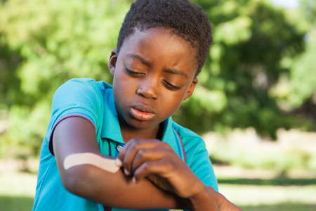 Little boy putting plaster on arm on a sunny dayの写真素材