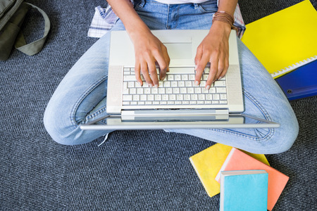 Student sitting on floor in library using laptop at the university