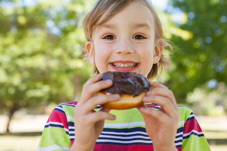 Little boy eating chocolate doughnut on a sunny dayの写真素材
