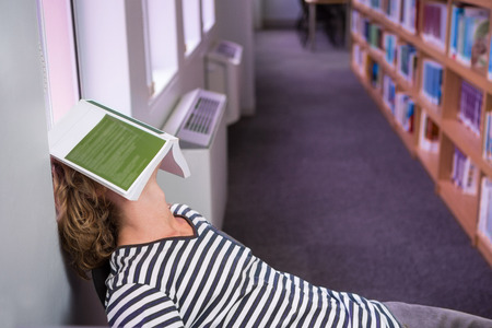 Student asleep in the library with book on his face at the university の写真素材