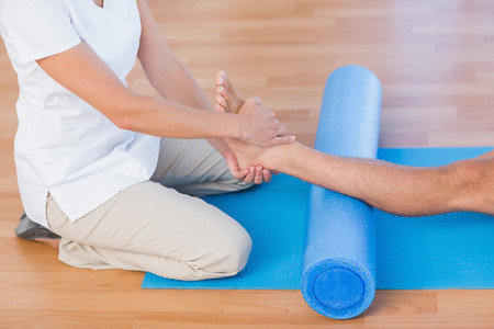 Trainer working with man on exercise mat in fitness studioの写真素材
