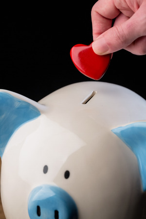 Hand putting heart in piggy bank shot in studioの写真素材