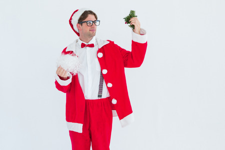 Geeky hipster in santa costume looking at mistletoe on white backgroundの写真素材
