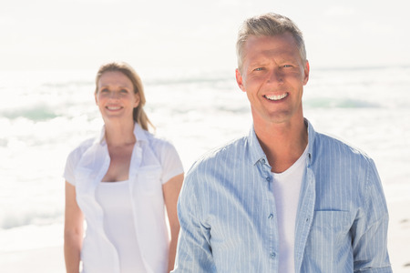 Happy couple smiling at camera at the beachの写真素材