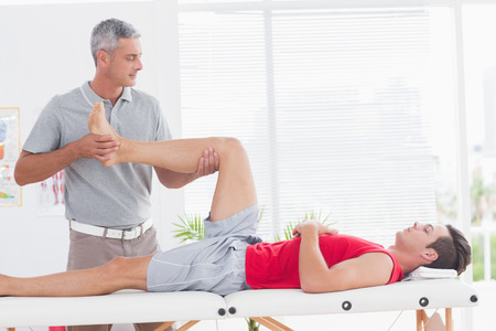 Physiotherapist doing leg massage to his patient in medical officeの写真素材