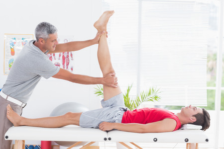 Physiotherapist doing leg stretching to his patient in medical officeの写真素材