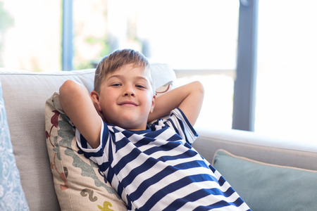 Little boy smiling on the couch at home in the living roomの写真素材
