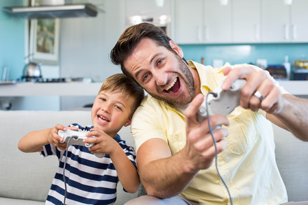 Father and son playing video games together at home in the living room
