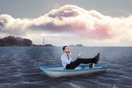 Businessman in boat with tablet pc against calm sea with lighthouseの写真素材