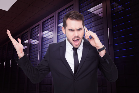Angry businessman gesturing on the phone against digitally generated server room with towersの写真素材