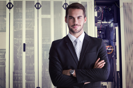 Smiling businessman posing with arms crossed against data center