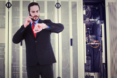 Serious businessman checking the time while on the phone against data center