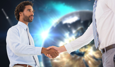 Young businessmen shaking hands in office against earth seen from spaceの写真素材