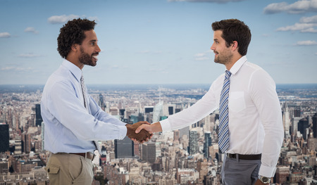 Smiling young businessmen shaking hands in office against new yorkの写真素材