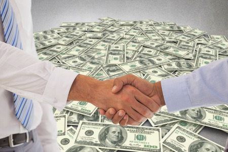 Close-up shot of a handshake in office against pile of dollarsの写真素材