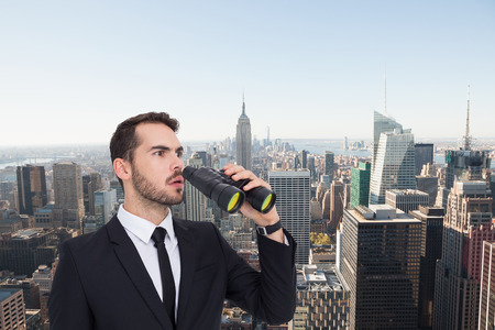 Surprised businessman standing and holding binoculars  against new yorkの写真素材