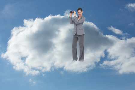 Businesswoman posing with binoculars against cloudy skyの写真素材